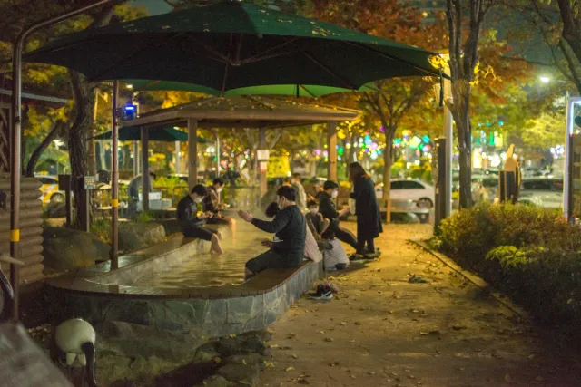 מבקרים יושבים ומשרים רגליים באגן מים חמים תחת שמשיות בערב