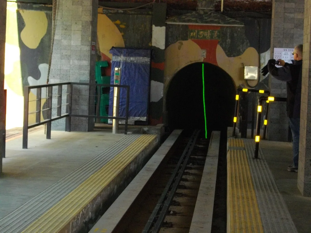 פתח מנהרה אפל עם מסילה יורדת אליו, בין קירות צבועים בהסוואה
