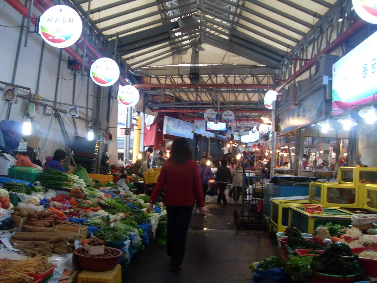 מעבר מקורה בשוק עם דוכני ירקות משני הצדדים ומנורות תלויות